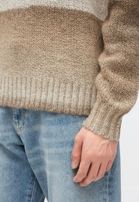 Stickad tröja med ett randigt mönster i beige och brunt, ribbade muddar och fåll. Kombinerad med ljusblå jeans i denim.