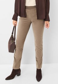 Beige corduroy pants with a stretchy waistband, paired with a dark brown blouse and ankle boots. Features a textured fabric and fitted design.