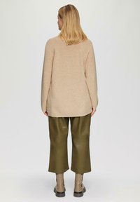 Beige gebreide trui met een relaxte pasvorm, lange mouwen en ribbelstructuur, gecombineerd met donker olijfgroene wijde broek en enkellaarsjes.