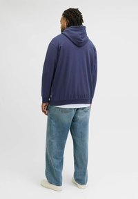 Mørkeblå hætte sweatshirt med en afslappet pasform, båret over en hvid skjorte. Lyseblå baggy jeans og off-white sneakers fuldender outfittet.