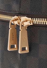 Brown textured material with gold zipper pulls featuring engraved logos. Zipper teeth align with the brown fabric, enhancing durability.