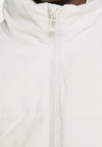 Chaqueta blanca con cremallera y collar alto. Cuenta con una cremallera frontal y un tejido ligero y suave. Diseño minimalista sin adornos.