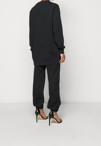 Svart sweatshirt och matchande joggingbyxor i mjukt tyg; avslappnad passform med ribbade manschetter. Knyts samman med svarta högklackade sandaler.