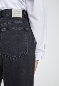 Jean mom en denim gris foncé avec une taille haute et une seule poche arrière, avec une étiquette verte portant l'inscription "Mom Jeans Pull&Bear".