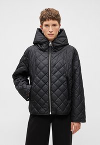 Melnā izšūta jaka ar augstu apkakli un priekšējo rāvējslēdzēju, divām sānu kabatām un pufa tekstūru siltumam.