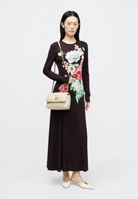 Czarna sukienka z długim rękawem w kwiatowy wzór w odcieniach niebieskiego i różowego, połączona z kremową torebką pikowaną i białymi czółenkami.