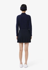 Camiseta polo de manga larga en color navy con una falda plisada a juego. Presenta una textura suave. Zapatillas blancas completan el conjunto.