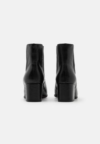 Bottines en cuir noir à texture lisse, talon bloc, avec des panneaux élastiques latéraux pour un enfilage facile. Design épuré et minimaliste avec une finition mate.