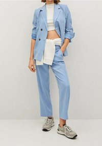 Světle modrý oblek na míru s dvouřadým sako a odpovídajícími kalhotami. Součástí outfitu je bílý top a šedé tenisky.