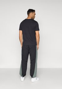 Juodas trumpomis rankovėmis marškinėliai derinami su laisvomis juodomis kelnėmis, turinčiomis žalias šonines juostas. Balti sportbačiai užbaigia aprangą.