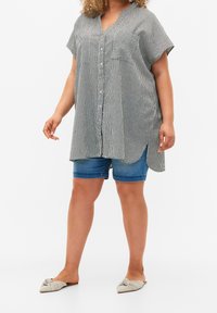 Black and white striped shirt with short sleeves, button front, and side slits, paired with blue denim shorts and patterned footwear.