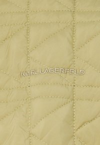 Quilted jakke i lys gul stof med diagonale syninger. Broderet "KARL LAGERFELD" logo i sølvtråd nær bunden.
