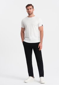 Hvid prikket t-shirt med rund halsudskæring og korte ærmer, parret med sorte bukser og hvide sportssko. Ingen tydelige mønstre eller accenter.