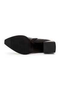 Chaussure en cuir noire vue de la semelle, avec un bout pointu, une semelle texturée antidérapante et un petit talon bloc sur fond blanc.