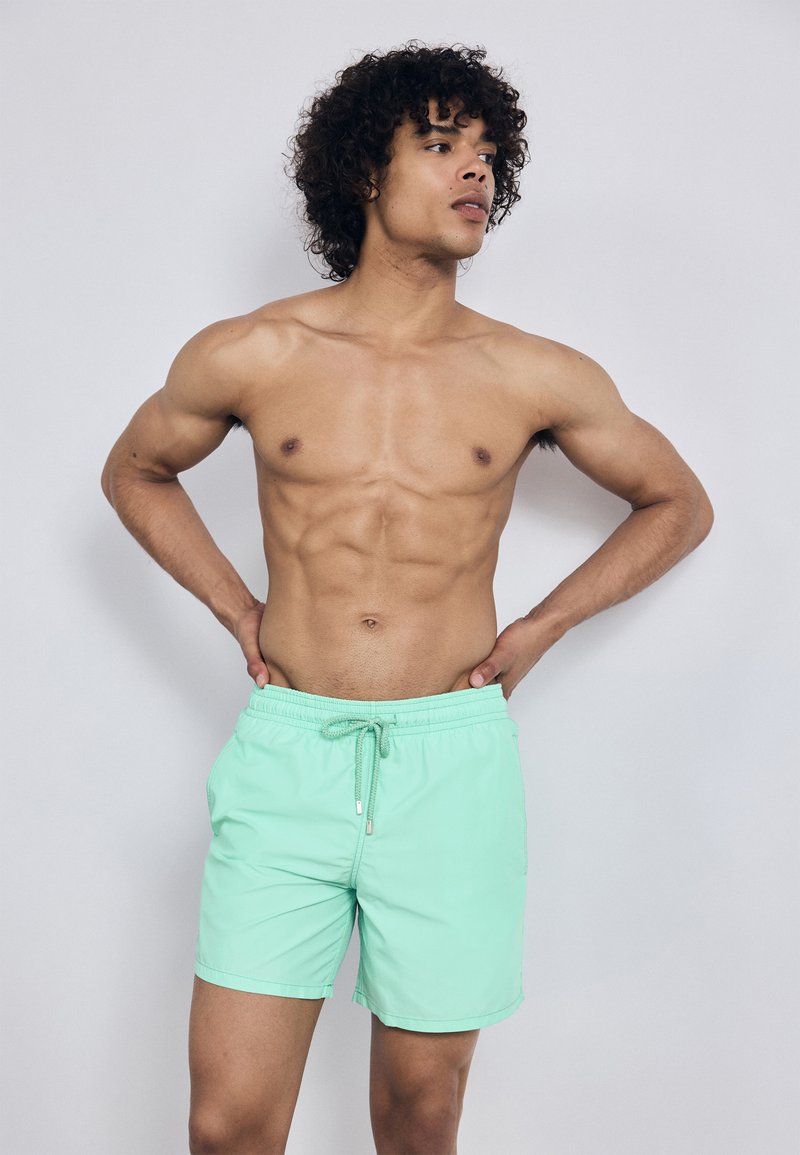 Μακρύ κολυμβητήριο σορτς σε μέντα πράσινο χρώμα με ελαστική μέση και κορδόνι. Το υλικό φαίνεται ελαφρύ και λείο, σχεδιασμένο για χρήση στο νερό.