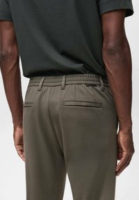 Slim-fit, elastic-waist trousers in olive green fabric. Features two back pockets, textured surface, and a clean, tailored design.