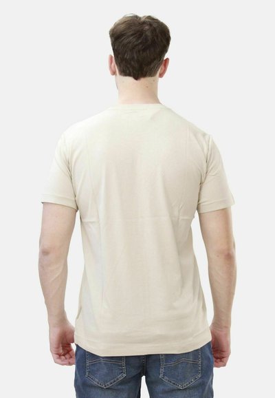 Beige short-sleeve T-shirt with a round neck, made of soft cotton. Plain design, smooth texture, and a relaxed fit, worn with blue jeans.