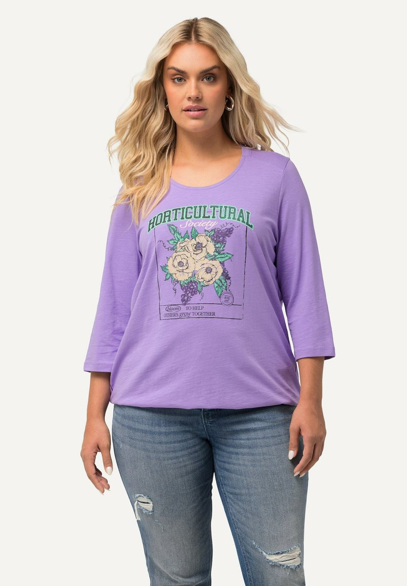 Camiseta de manga tres cuartos en color lavanda con un gráfico floral y el texto 'Sociedad HORTICULTURAL' en verde. Material de algodón suave, corte relajado.