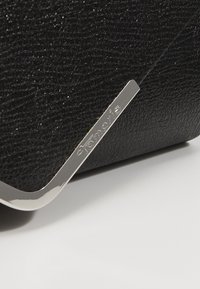 Musta tekstuuripinnaline nahk käekott, millel on hõbedane metallaktsent. Omab sujuvat ristkülikukujulist disaini ja küljes on logo silt.