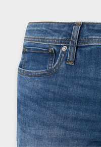 Τζιν παντελόνια σκουρόχρωμου ντενίμ με κοντράστ ραφές, σχεδιασμό με πέντε τσέπες και μεταλλικό κουμπί. Το ύφασμα παρουσιάζει ένα απαλό, ελαφρώς υφασμένο φινίρισμα.