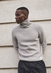 Pulover slim fit de culoare gri deschis, cu guler înalt, dintr-un material texturat, cu mâneci raglan și o etichetă mică la margine.