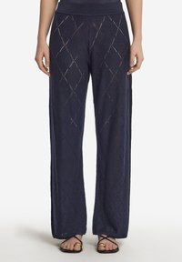 Marinblå vida byxor i strukturerad, mönstrad tyg med diamantformade utskärningar, avslutade med ett bekvämt midjeband och kombinerade med platta sandaler.