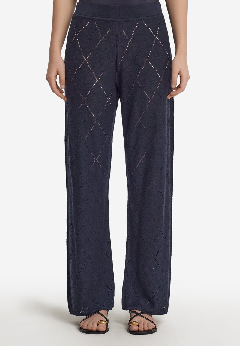 Marinblå vida byxor i strukturerad, mönstrad tyg med diamantformade utskärningar, avslutade med ett bekvämt midjeband och kombinerade med platta sandaler.