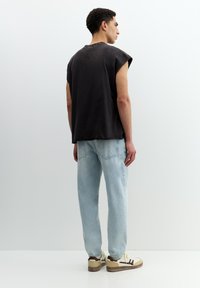 Schwarz ärmelloses T-Shirt mit rohen Kanten, kombiniert mit hellblauen geraden Jeans und beigen Turnschuhen mit dunklen Akzenten.
