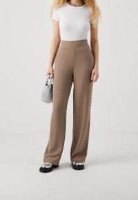 High-waisted brown trousers in lightweight fabric, wide-leg design, paired with a fitted white top and chunky black platform shoes.