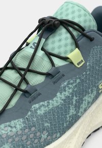 Αθλητικό παπούτσι με ανάγλυφη επάνω επιφάνεια σε μέντα πράσινο χρώμα, σκουρότερες τιρκουάζ λεπτομέρειες και μαύρα κορδόνια. Διαθέτει σχέδιο με μοτίβο στην εξωτερική επιφάνεια και ελαφρύ σχεδιασμό.