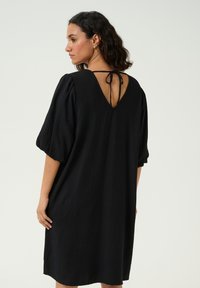 Black dress made of lightweight fabric, featuring a loose fit, puffed sleeves, and a V-back with a tie closure. Smooth texture.