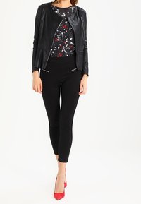 Black leather jacket over a star-patterned top, paired with black fitted pants and red high heels. Zipper accents on the jacket detail.