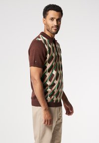 Camisa polo de manga corta en marrón con un patrón geométrico en crema y verde, que presenta un cuello con solapa y un dobladillo acanalado.