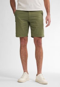 Green cotton shorts with a straight cut, side pockets, and a smooth texture, paired with off-white sneakers.