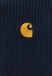 Μπλε ριγέ κάλτσες με κεντημένο κίτρινο στροβιλιστό λογότυπο. Η εστιασμένη υφή και η αντίθεση χρωμάτων αναδεικνύουν το σχέδιο και τη λεπτομέρεια της μάρκας.