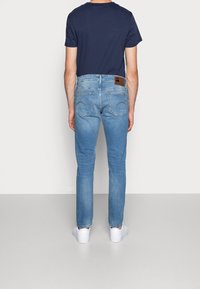 Ljusblå jeans i denim med smal passform, bakfickor med dekorativ sömnad och en brun läderlogotyp på midjebandet. Kombinerade med en marinblå t-shirt och vita sneakers.