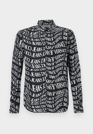 Črna majica z večkratnim belim napisom, ki vsebuje "VERSACE" in "JEANS", dolgimi rokavi in standardnim ovratnikom. Gladek teksturiran material.