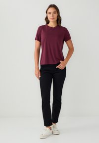 Bordeaux t-shirt met korte mouwen en een ronde hals, gecombineerd met zwarte slim-fit broek en witte sneakers. Zachte stof met een ontspannen pasvorm.