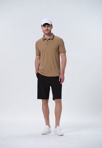 Polo de color marrón claro con un cuello negro en contraste, combinado con pantalones cortos negros y zapatillas blancas. La tela parece suave y ligera.