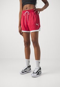 Pantalones cortos deportivos rojos con detalles en blanco, que cuentan con una cinturilla elástica y cordón, combinados con zapatillas negras y blancas y calcetines hasta la mitad de la pantorrilla.