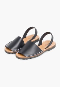 Sandali slingback in pelle nera con un ampio cinturino e design aperto sulla punta. Presentano una soletta color marrone chiaro e cuciture bianche lungo il bordo. Suola in gomma.
