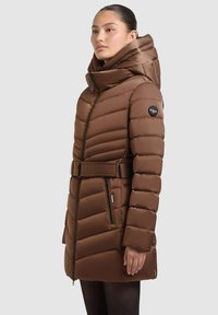 Smeđi prešani puffer kaput s visokim ovratnikom i remenom, s patentnim zatvaračem na džepovima i logotipom na rukavu. Glatka, sjajna tekstura.