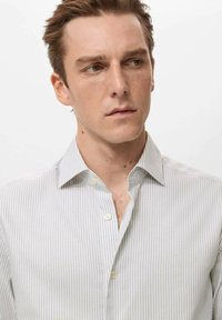 Camisa de botones a rayas en gris claro y blanco, con un collar puntiagudo, hecha de una tela suave, que presenta una textura sutil y botones en la parte delantera.