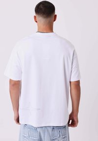 Witte T-shirt met korte mouwen en een ronde hals. Heeft een subtiele stervormige borduring nabij de zoom. Gemaakt van een soepel, lichtgewicht stof.