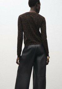 Camiseta de manga larga con estampado de leopardo marrón combinada con pantalones de cuero negros de pierna ancha. La camiseta tiene un escote redondo y mangas ajustadas.