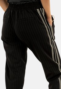 Zwarte broek met streepjes, voorzien van een elastische tailleband, met zijzakken en witte zijpanelen voor contrast. Gladde stofstructuur.