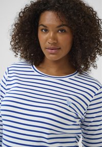 White long-sleeve top with blue horizontal stripes, featuring a small blue heart embroidery on the chest. Soft cotton material.