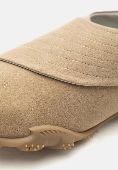 Μπεζ δερμάτινο παπούτσι σουέτ με οριζόντιες και κάθετες ραφές και υφασμένο πέλμα με μικρές καουτσούκ ακίδες για καλύτερη πρόσφυση.