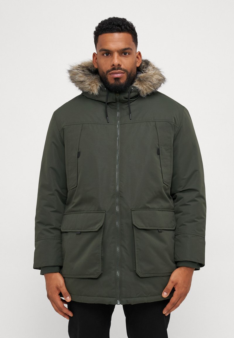 Parka verde con capucha forrada de piel, cierre de cremallera, dos bolsillos delanteros con solapa y cordones ajustables. La tela tiene una textura suave.