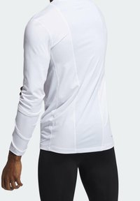Långärmad träningsskjorta i vitt, tillverkad av ett andningsbart tyg med strukturerade paneler och en åtsittande design. Har sömlösa ärmar och rund halsringning.